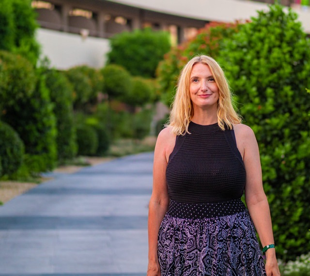Image shows Marianne Rawlins the guest of this episode standing in the foreground of the photo smiling at the camera