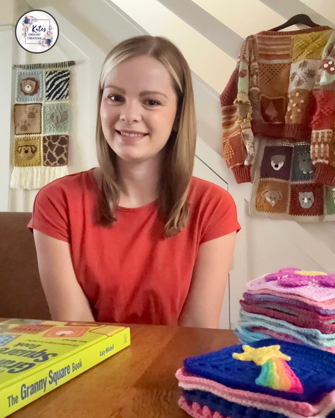 Image shows Katy Mitchell from Kate's Crochet Creations sitting at a table surrounded by crocheted items and her book about Granny Squares